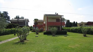 Zona residencial amb una casa de dos pisos, façana vermella i beix, envoltada per jardins i taronjades ben cuidats.