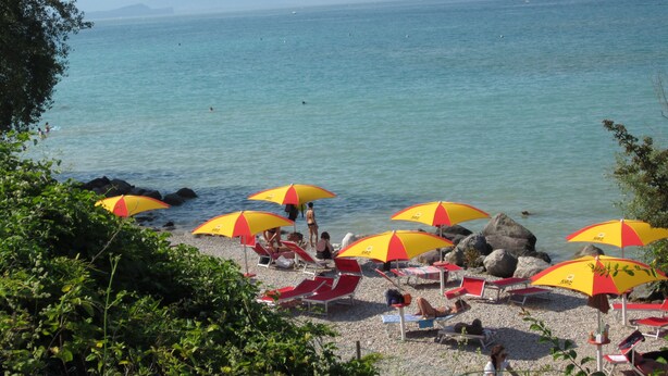 Una platja amb ombrel·les vermelles i grogues, gandules i terreny rocos.