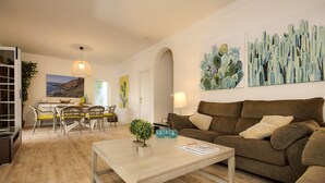 Een woonkamer met een bruine bank, een houten salontafel en een eethoek met een tafel en stoelen.