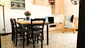 Uma sala de jantar com uma mesa de madeira, cadeiras, um vaso de planta, uma televisão e um relógio na parede.