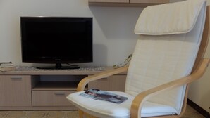 Quarto moderno com uma cadeira de madeira, uma televisão de tela plana e uma escrivaninha pequena.