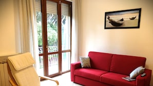 Um sofá vermelho, uma cadeira de madeira com uma revista, e um quadro de um barco na praia.