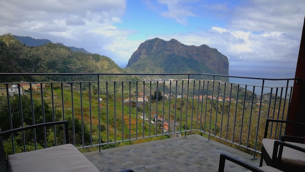A balcony with a view of a mountainous landscape and a village below.