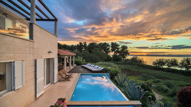 Piscina com vista para o pôr do sol, área de varanda coberta e jardim bem cuidado.