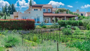 Uma casa grande com piscina, rodeada por jardins exuberantes e um céu azul límpido.