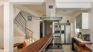 Cozinha moderna com ilha central, eletrodomésticos de aço inoxidável e bancada de madeira.
