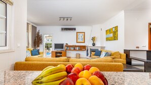 Ett vardagsrum med en soffa, en tv, en bokhylla och en skål med frukt på en bänkskiva av granit.