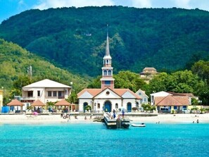 Un pueblo costero con una iglesia destacada, playa y montañas al fondo.