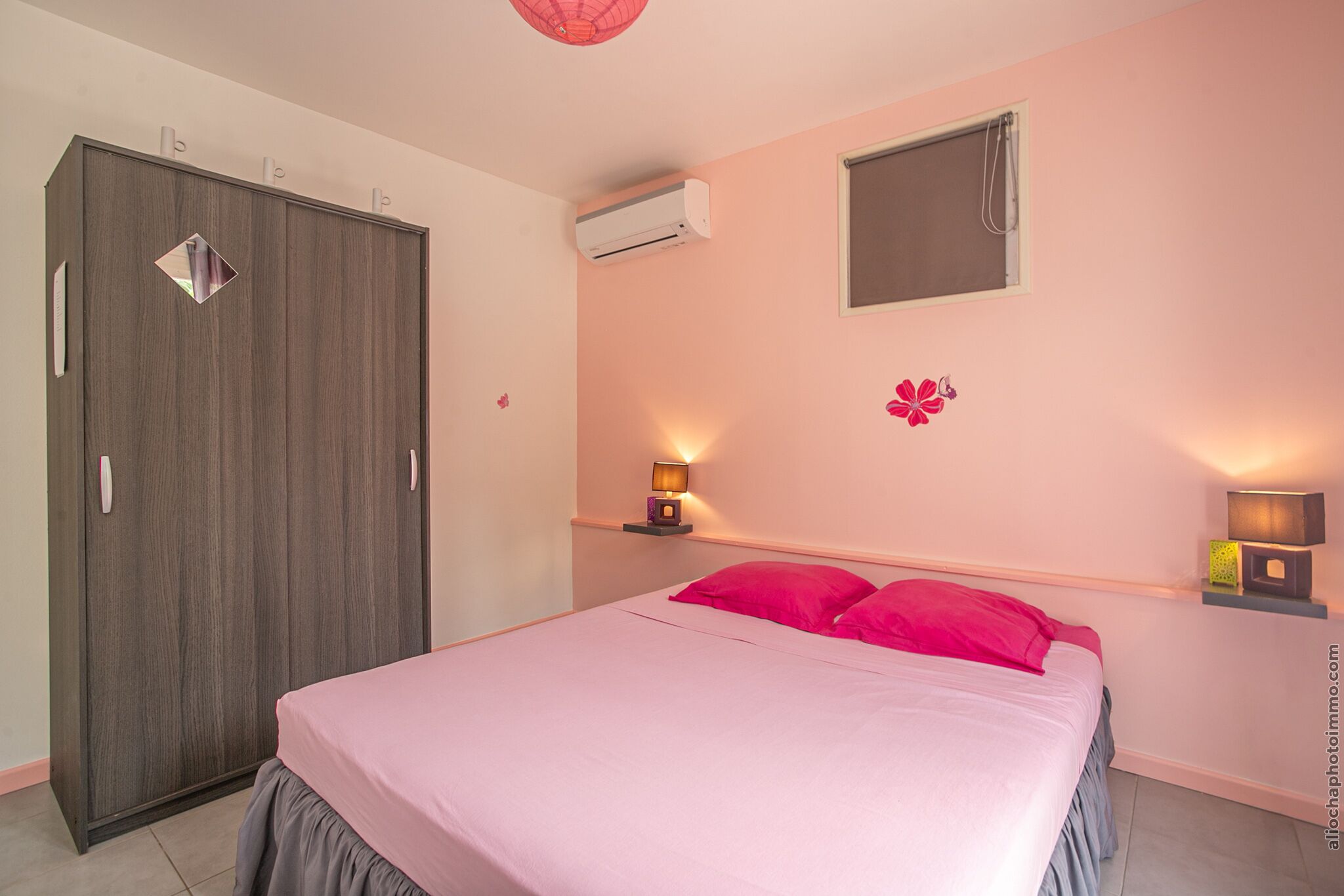 A bedroom with a bed, a wardrobe, an air conditioner, a window, and wall-mounted lights.