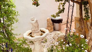 Un jardín con una fuente de piedra, una estatua y diversas plantas.