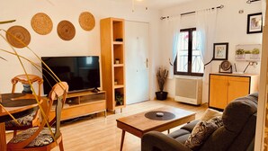 Una sala de estar con televisor, muebles de madera, ventilador de techo y una ventana con cortinas.