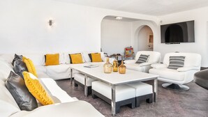 Ein modernes Wohnzimmer mit weißen Sofas, einem zentralen Couchtisch und einem an der Wand montierten Flachbildfernseher.