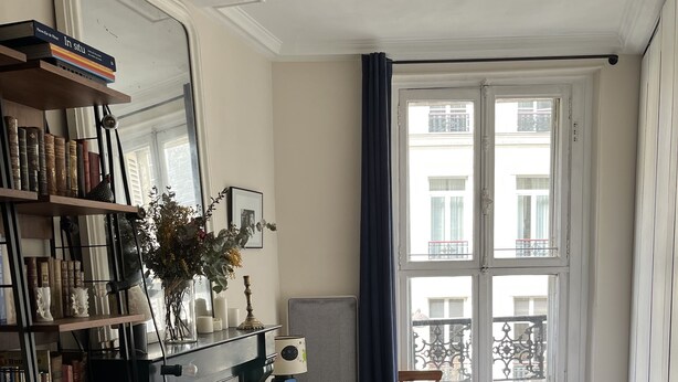 Une chambre à coucher comprenant un lit, une commode, une bibliothèque, une cheminée et une fenêtre donnant sur des immeubles.