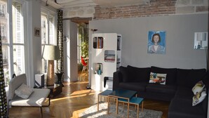 Un salon avec un canapé noir, une petite table en bois, une chaise et une bibliothèque.