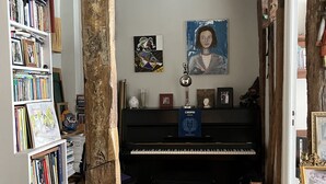 Une pièce avec un plancher en bois, un piano noir, une bibliothèque et un tableau accroché au mur.