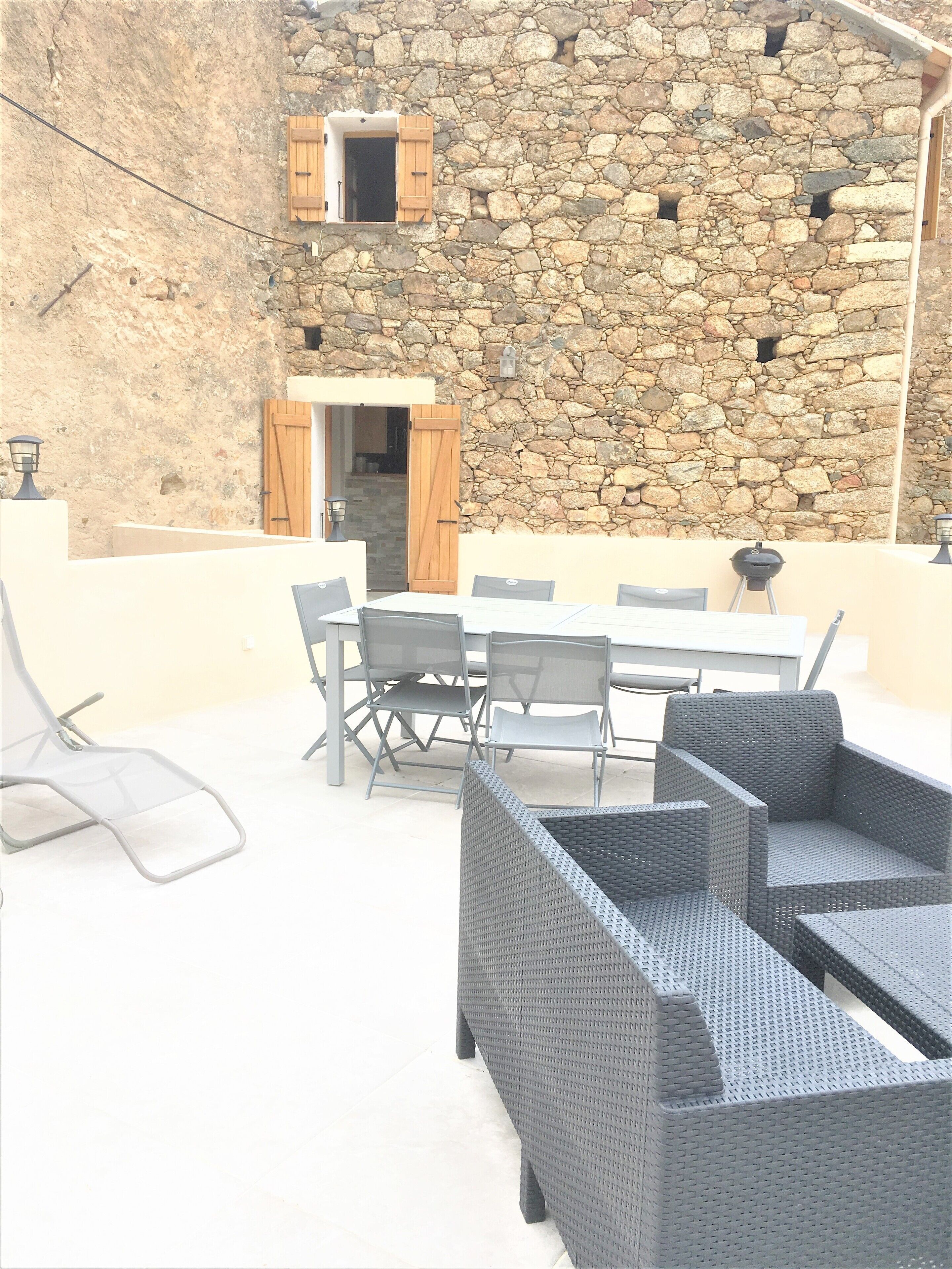 Een terras buiten met stenen muren, een tafel, stoelen en een rieten bank.