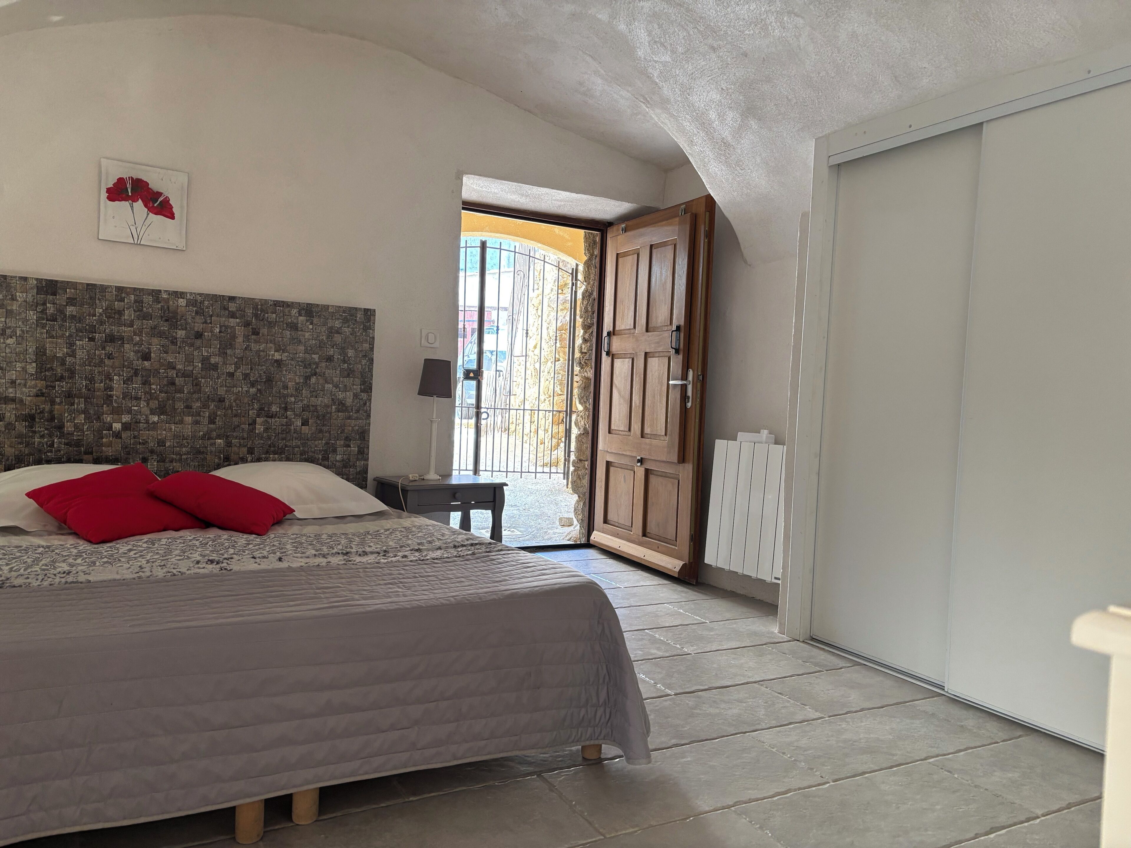 A bedroom with a bed, a nightstand, a lamp, and a door leading to a balcony.