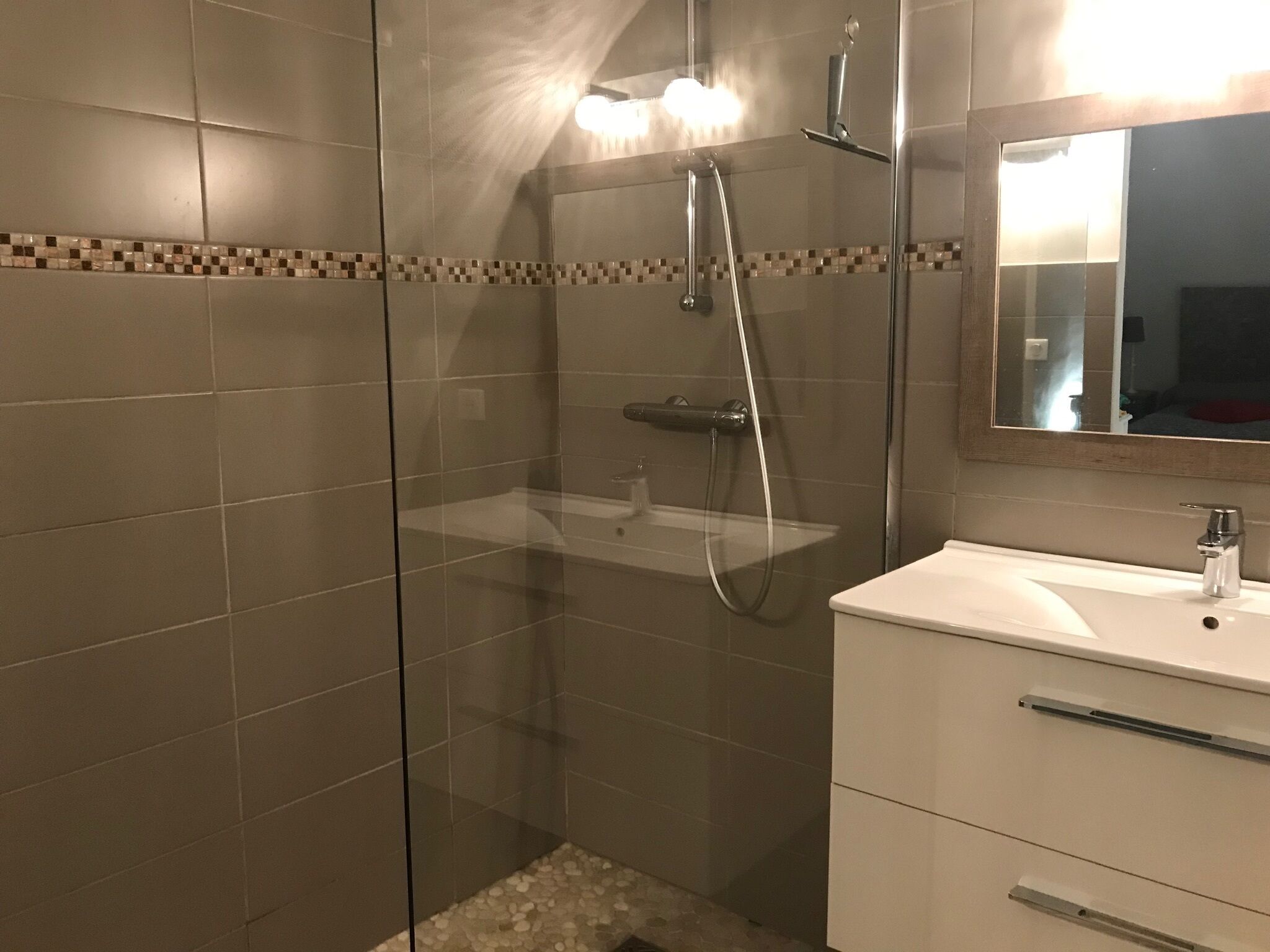 Un baño moderno con cabina de ducha de vidrio, un lavamanos blanco y un espejo sobre el lavabo.