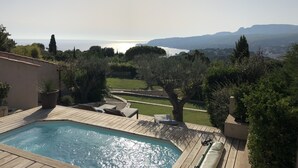 A swimming pool with a wooden deck, surrounded by greenery and overlooking a scenic view of the sea and distant hills. - Luxury Villa 5 * - Cassis (Cassis)
