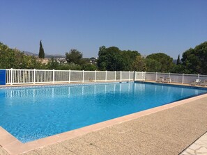 Ein rechteckiger Pool mit weißem Zaun und Liegestühlen am Rand.