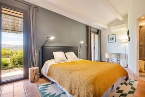 Ein Schlafzimmer mit Bett, Nachttisch, Lampe, Stuhl und Blick ins Freie.