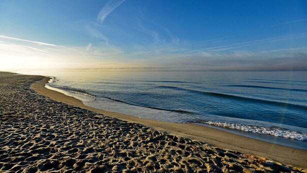 A beach with a wide sandy area and gentle waves.