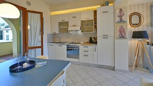 A modern kitchen with white cabinets, a built-in oven, and a dining area with a table and chairs.