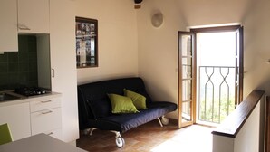 A compact kitchen with a built-in stove, a sofa with green cushions, and a sliding glass door leading to a balcony.
