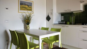 A modern kitchen with white cabinets, a green backsplash, and a dining area with a white table and green chairs.