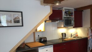 A kitchen with red cabinets, a wooden stool, a microwave, and a toaster. - Apartment in Beautiful Alpine Village (Chamonix-Mont-Blanc)