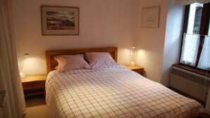 A bedroom with a bed, two bedside lamps, a framed picture on the wall, and a window with curtains. - Apartment in Beautiful Alpine Village (Chamonix-Mont-Blanc)