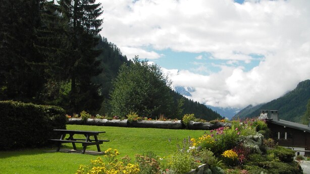 A picnic area with a bench, surrounded by a well-maintained garden with various flowers and a stone wall. - Apartment in Beautiful Alpine Village (Chamonix-Mont-Blanc)
