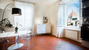 Une cuisine moderne dotée d’une grande fenêtre, de meubles blancs et d’un coin repas avec des chaises transparentes.