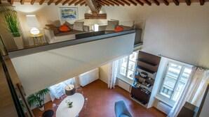 Un vaste espace de vie doté d’un haut plafond, comprenant une table à manger avec des chaises, un canapé et un fauteuil bleu.