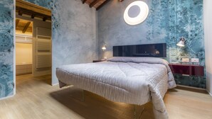 Une chambre à coucher avec un lit, des poutres en bois au plafond, un luminaire rond et un papier peint à motifs.
