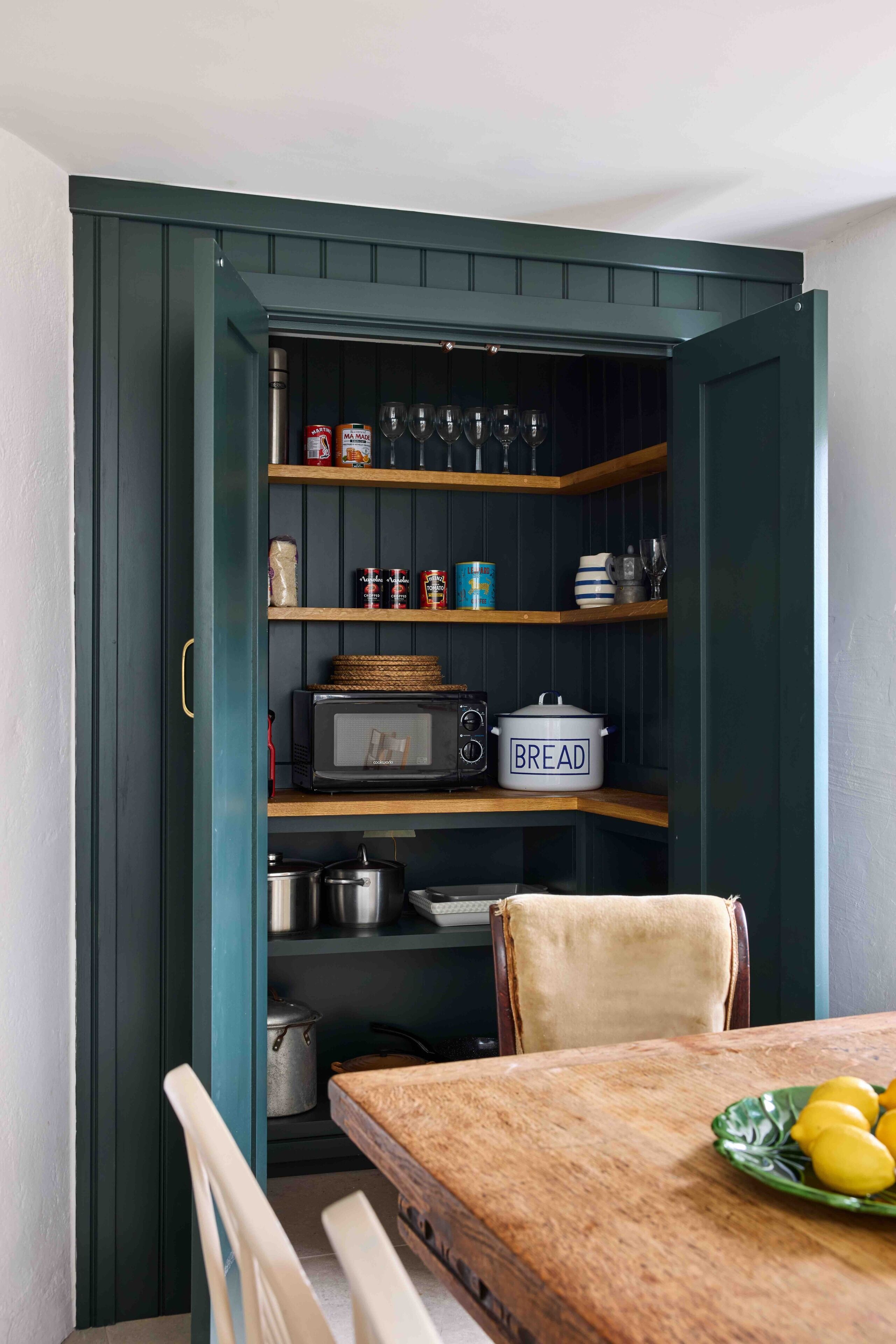 A kitchen with a dark green cabinet, a microwave, a bread container, and a table with a plate of lemons.