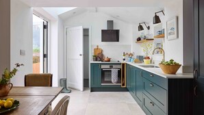 A modern kitchen with teal cabinets, a built-in oven, and a large window. - Beautiful cottage with sea views and private beach access (Helston)