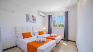 Ein Hotelzimmer mit zwei Betten, weißer Bettwäsche, orangefarbenen Akzenten, einem Fenster mit Vorhängen und einer Klimaanlage.