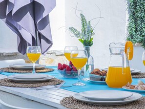 A table set for breakfast with plates, glasses, a pitcher of orange juice, a bowl of fruit, and muffins.