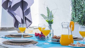 A table set for breakfast with plates, cutlery, a bowl of fruit, a pitcher of orange juice, and a vase with flowers.