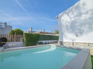 A swimming pool with a wooden deck and a white wall.