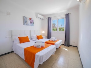 A hotel room with two beds, a window with curtains, an air conditioning unit, and artwork on the wall.