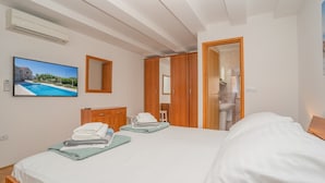 A bedroom with a bed, a TV, a mirror, a wardrobe, and a bathroom visible through an open door.