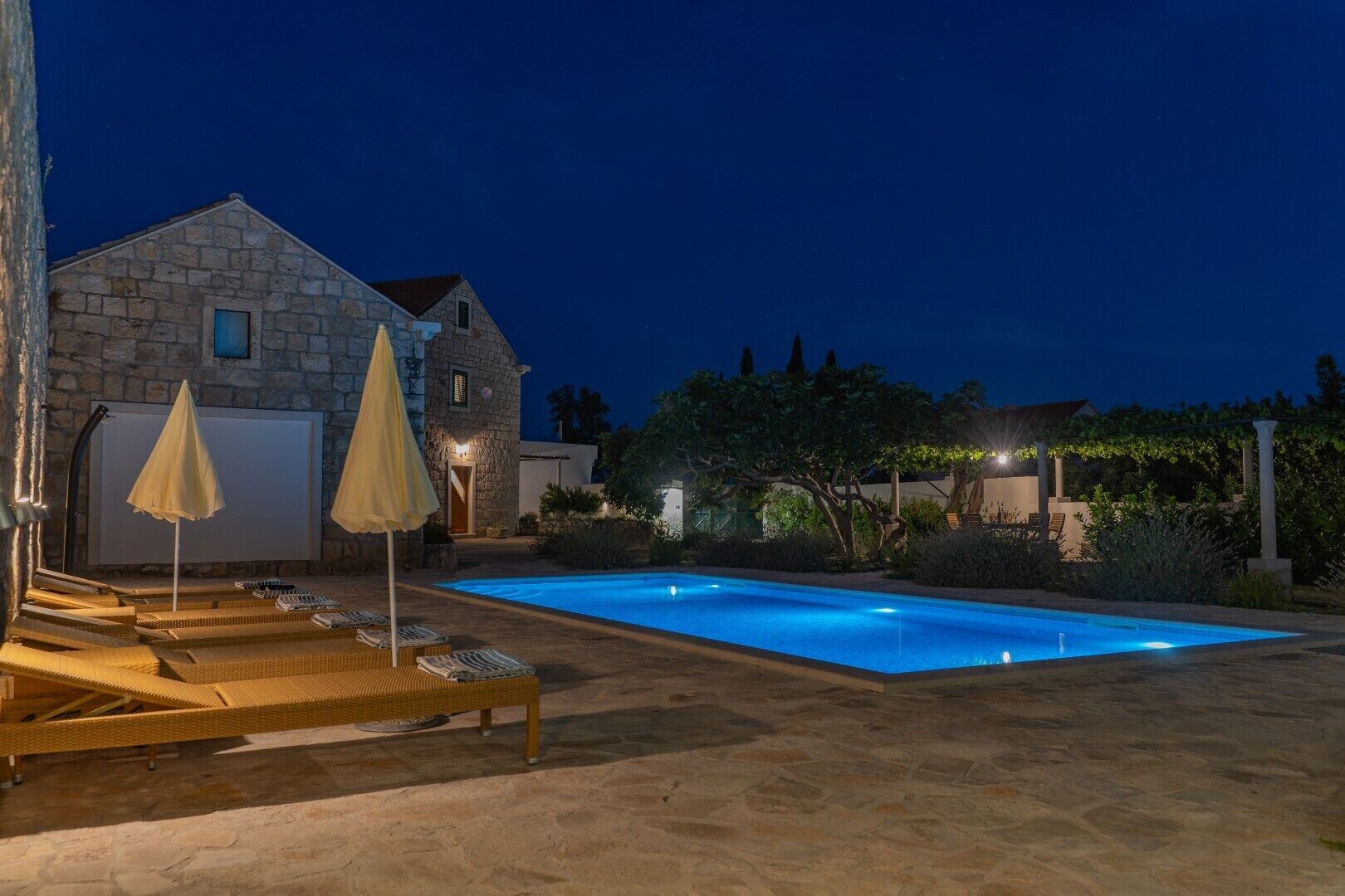 Ein Steinhaus mit Swimmingpool, Sitzgelegenheiten im Freien und einem gut beleuchteten Garten bei Nacht.