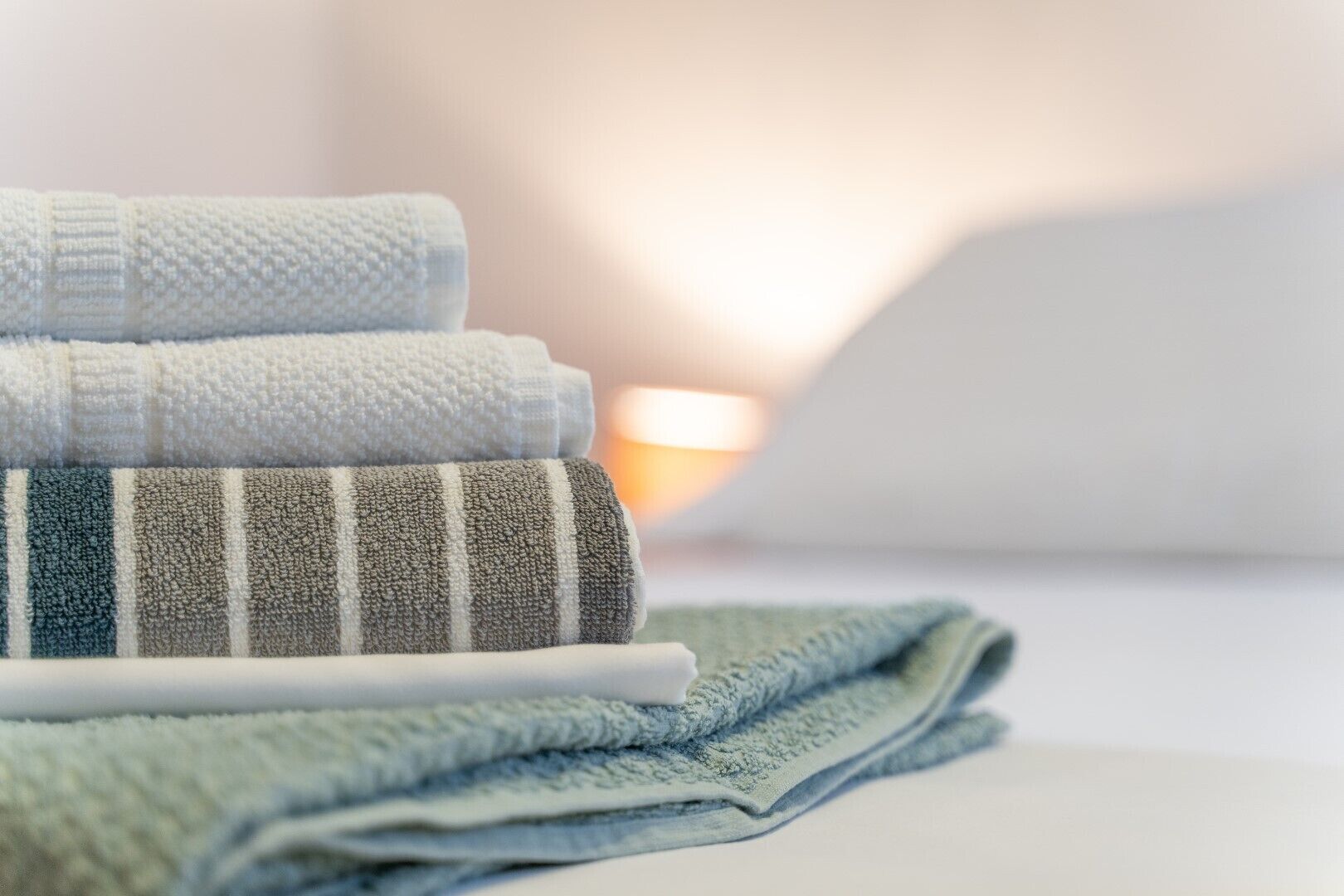 A stack of folded towels in various colors and patterns, placed on a white surface.