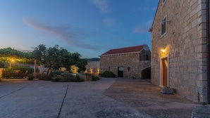 A stone building with a red-tiled roof, a paved courtyard, and outdoor seating.