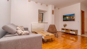 A living room with a sofa, a coffee table, a wicker chair, a TV, and a painting on the wall.