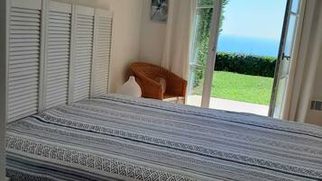 Une chambre à coucher avec un lit, une chaise, une fenêtre donnant sur un paysage et un mur orné d’une horloge.