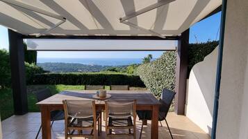 Une terrasse extérieure avec une table et des chaises, une vue sur la mer et un espace abrité agrémenté d’une pergola.