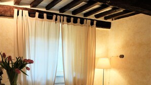 A room with a bed, a lamp, a vase with flowers, and a window with curtains. - Ancient house in the hill with a garden and view to the sea. Wi-Fi free (Camaiore, Lucca)